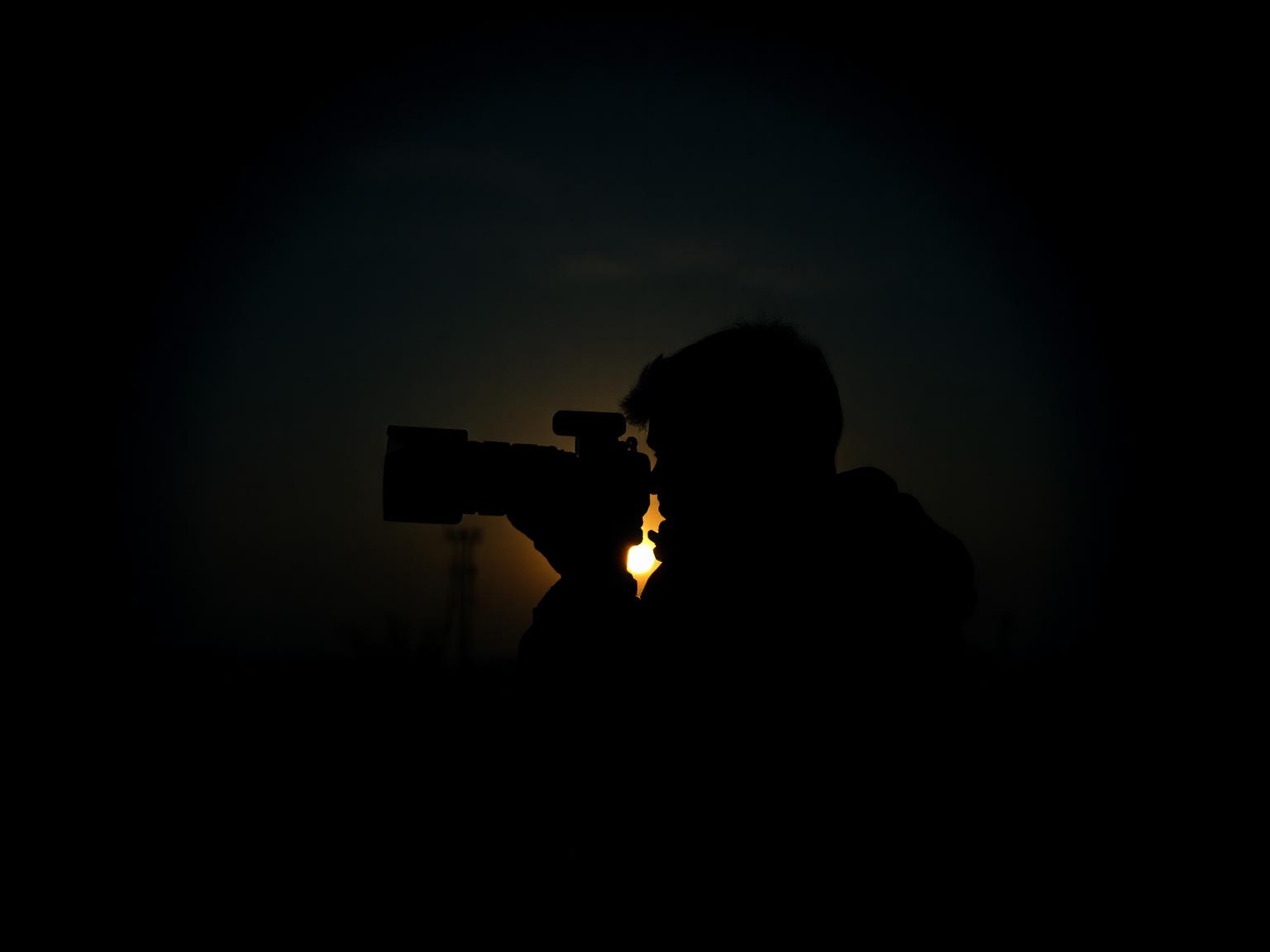 Photographer silhouetted against a setting sun, viewed through a simulated viewfinder